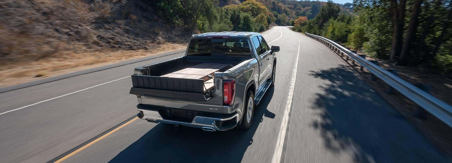 Pickup truck with open bed driving on a scenic, winding road lined with trees.