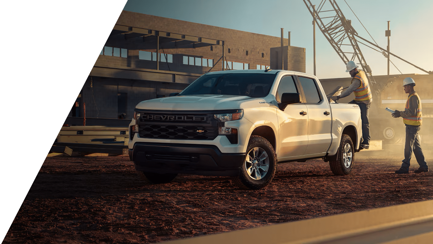 White Chevrolet pickup truck at a construction site with workers and equipment in the background.