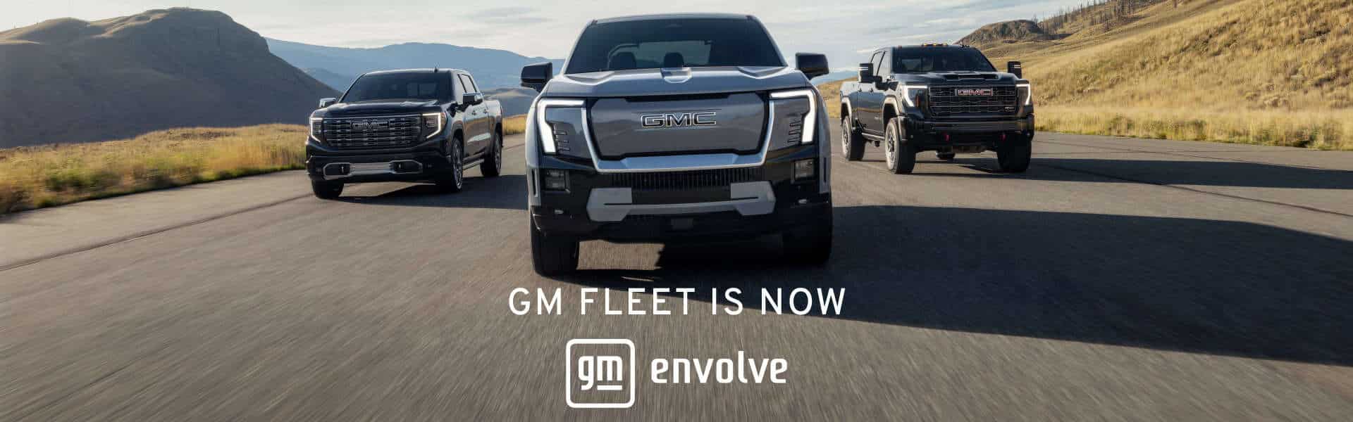 Three GMC trucks driving on a scenic road, promoting "GM Fleet is now GM Envolve."