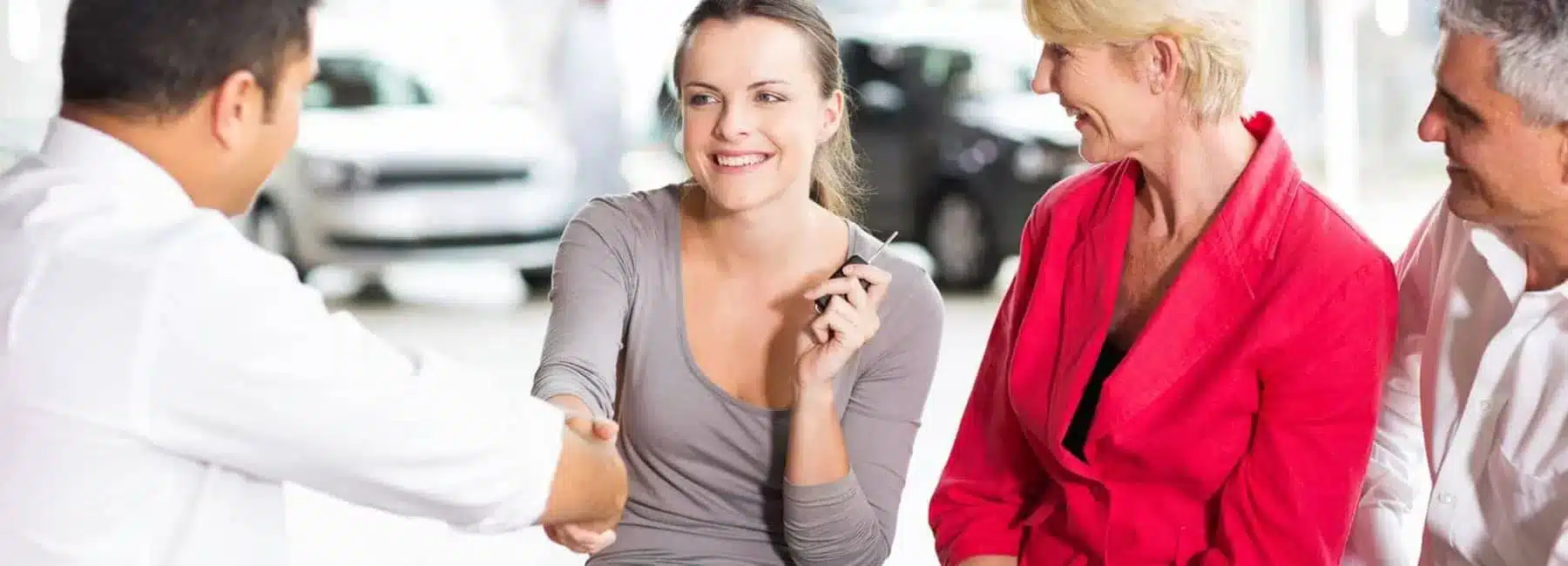 Woman smiling and shaking hands at a car dealership with three people chatting.