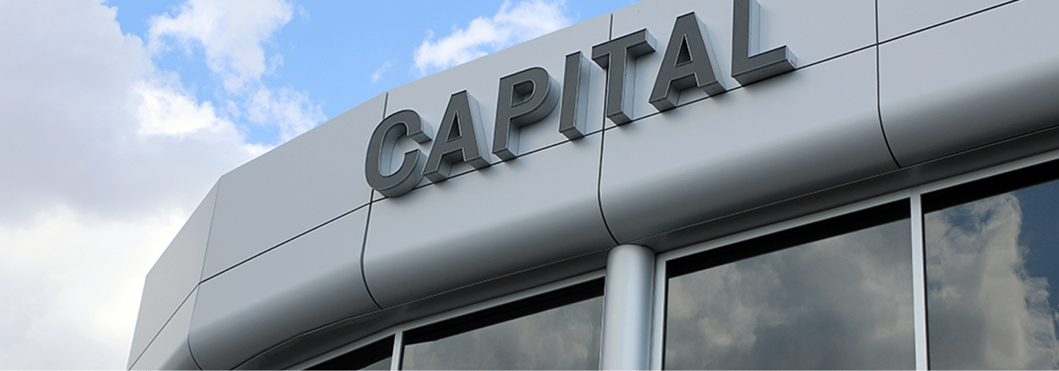 Modern building facade with "CAPITAL" sign and reflective windows under a cloudy sky.