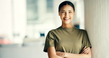 Smiling person in a green shirt stands with arms crossed against a blurred indoor background.
