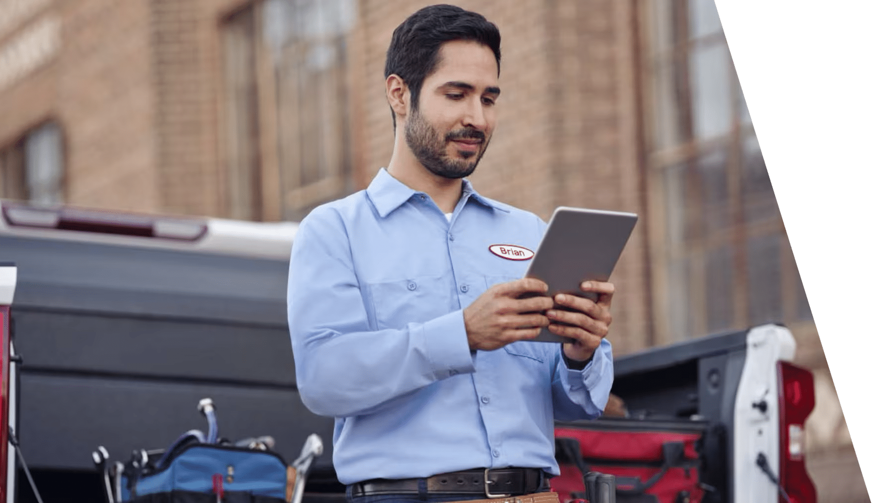 Technician in a blue shirt using a tablet near a truck, with tools visible in the background.