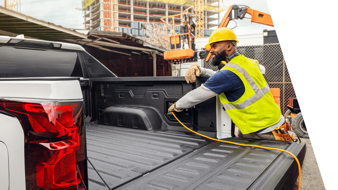 Construction worker in safety gear connects equipment in a truck bed at a building site.