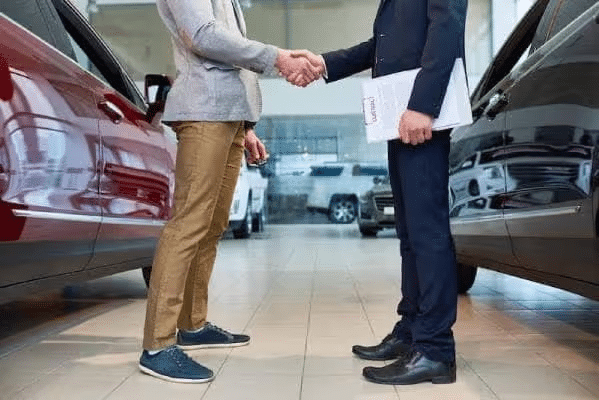 Two people shaking hands in a car showroom, symbolizing a successful car sale.