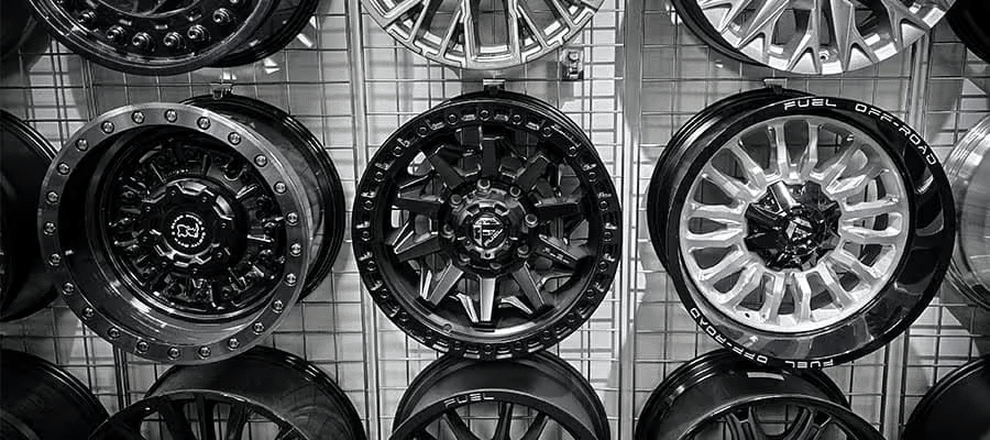 Various styles of car rims displayed on a wire grid, featuring black and silver designs.