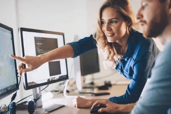 Woman pointing at computer screen while discussing with a colleague.