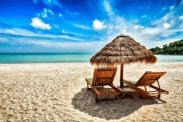 Tropical beach with two lounge chairs under a thatched umbrella, overlooking clear blue ocean and skies.