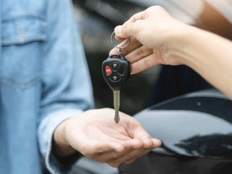 Hand passing a car key with remote to another person, symbolizing car purchase or rental.